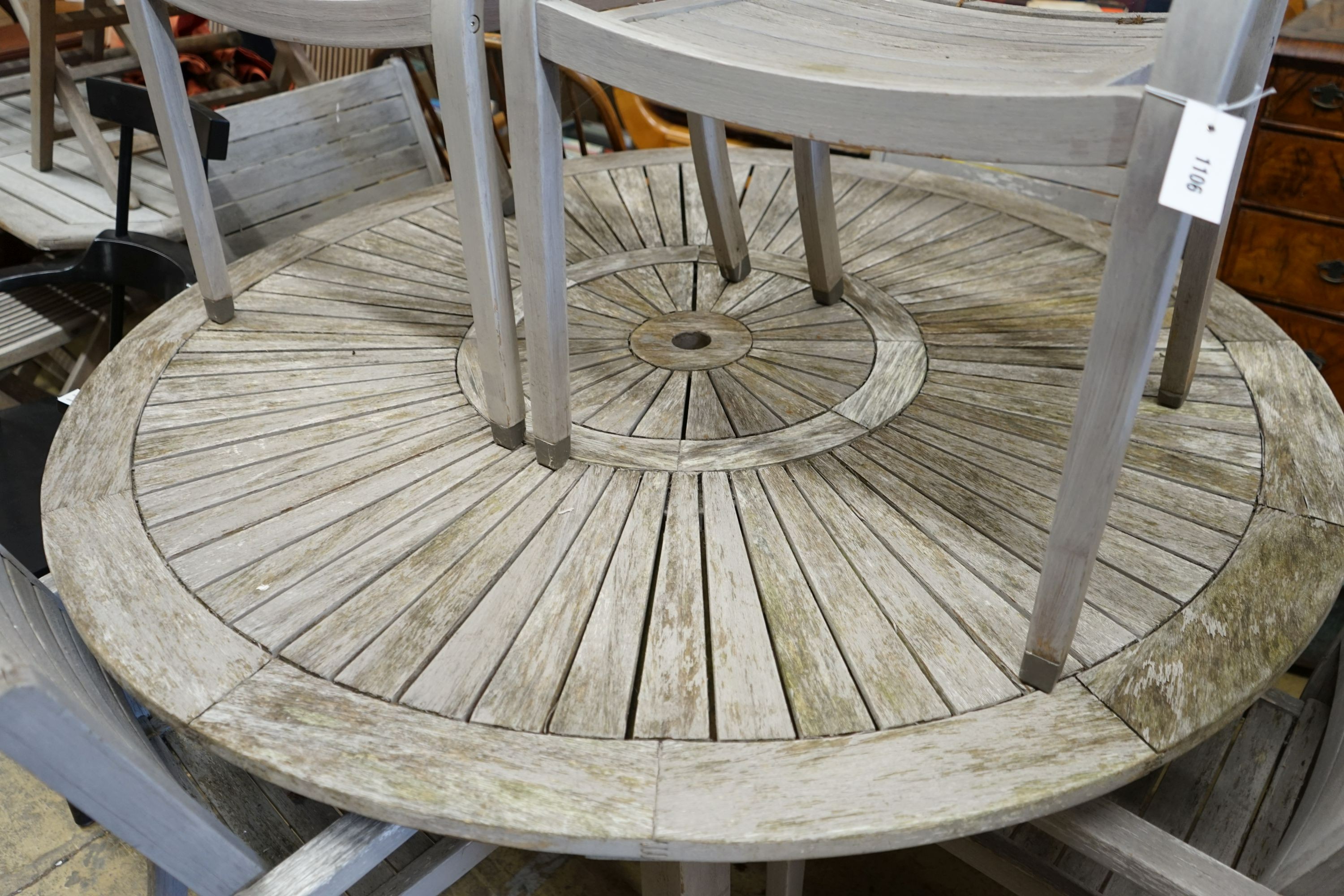 A circular weathered teak garden table, diameter 153cm, height 75cm together with six weathered teak stacking garden elbow chairs